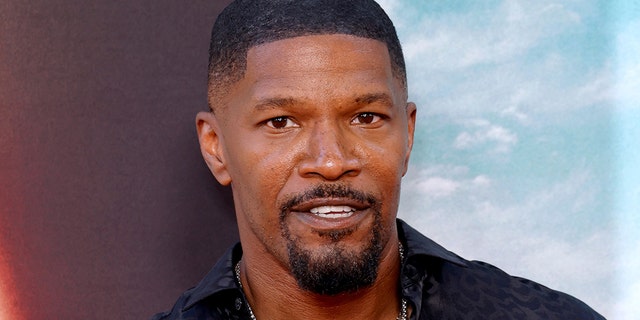 Jamie Foxx smiles on the carpet in a black shirt in Los Angeles