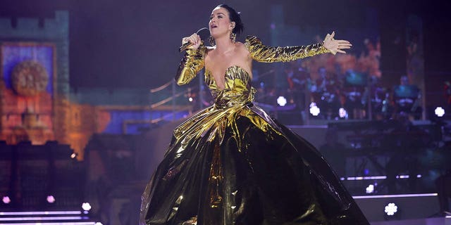 Katy Perry wore a strapless foil-like gold dress and separate long sleeve gold arms while singing into a microphone on stage during the coronation concert