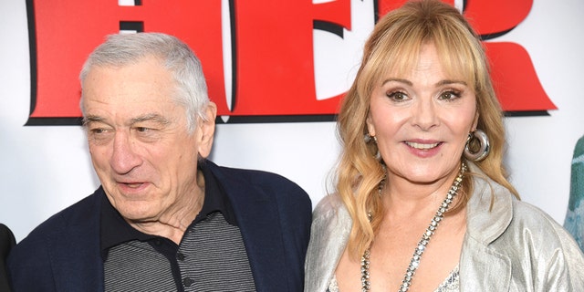 Robert De Niro looks to his right on the red carpet of his new film "About My Father" with co-star Kim Cattrall in a sparkly outfit with a deep V cut