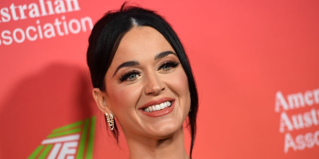 Katy Perry flashes a smile on the red carpet in a gown with her hair pulled back