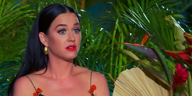 Katy Perry in a cheetah print tank top with red bows looks perplexed while watching a performance during "American Idol"