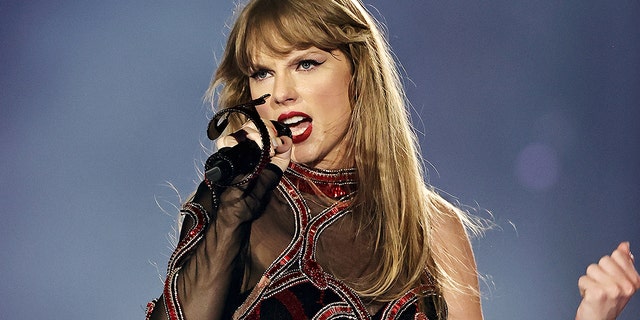 Taylor Swift in her 'Reputation' era jumpsuit sings into a microphone while on stage at the Era's Tour