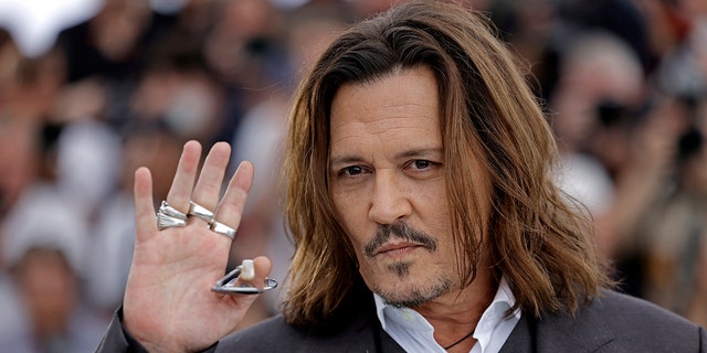 Johnny Depp holds up his right hand with lots of silver rings and waves to the crowd in Cannes with a slight smirk/smile on his face