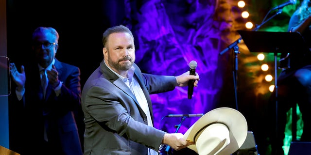 Garth Brooks performing onstage holding a microphone and his hat.