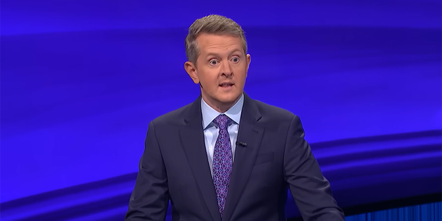 Ken Jennings in a navy suit with a light blue shirt and purple suit on the set of 'Jeopardy!'