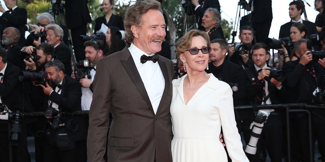 Bryan Cranston wearing a suit and bowtie on the red carpet with his wife Robin wearing a white dress