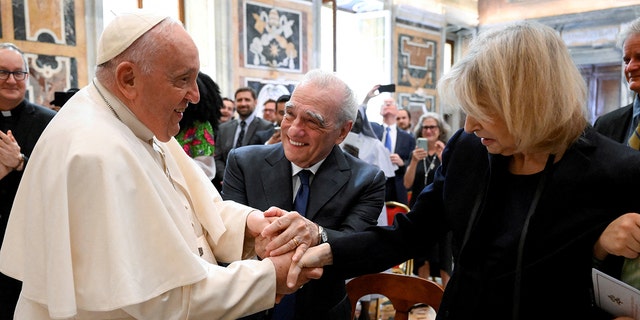 Pope Francis in his white robe holds the hands of Martin Scorsese's wife Helen as Martin looks on and adds his hand to the pile