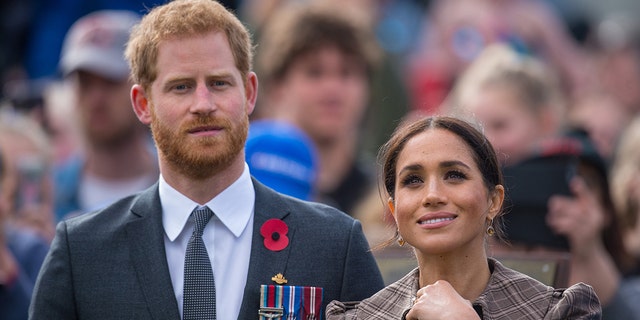 Meghan Markle wearing a brown dress looking up while standing next to Prince Harry wearing a suit and his medals