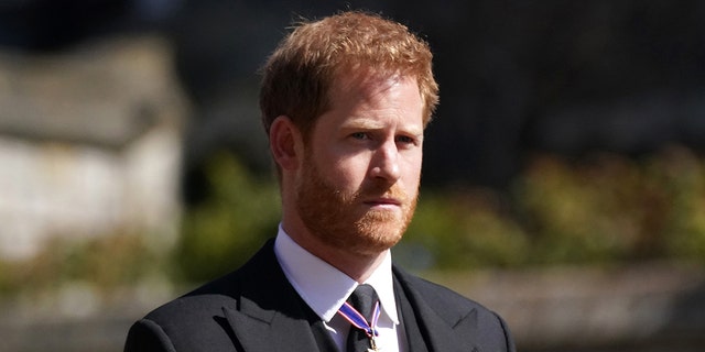 Prince Harry in a suit with medals looking sternly