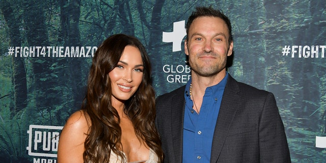 Megan Fox smiles on the red carpet with Brian Austin Green in a black jacket and blue shirt