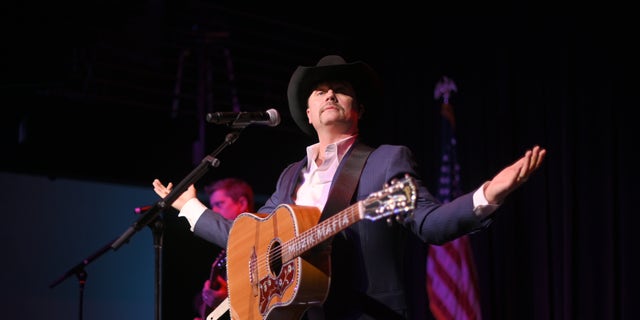 John Rich holds a guitar on stage during concert