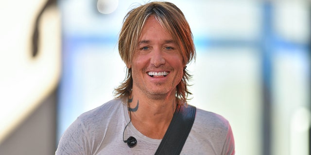 Keith Urban smiles on stage in New York City with a guitar slung across his back