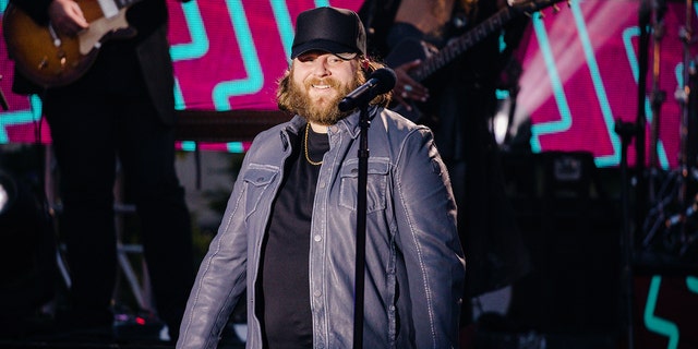 Nate Smith in a black hat and blue jacket performs on stage from the CMT Music Awards