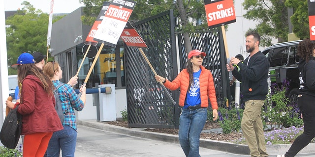 Justine Bateman in a red hat, blue shirt, and red jacket protests in Hollywood during the Writer's Strike