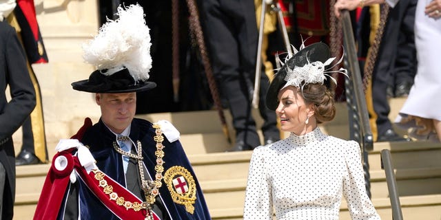 Kate Middleton and Prince William walk down steps wearing feathered hats.