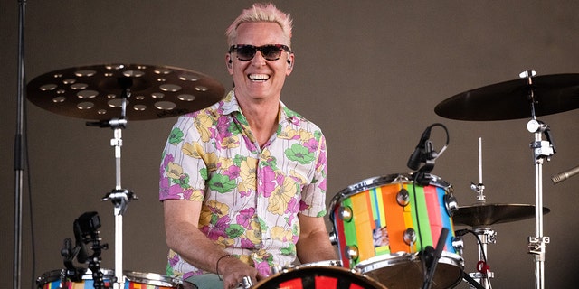Josh Freese in a colored patterned shirt smiles with sunglasses on behind a set of drums playing at Coachella