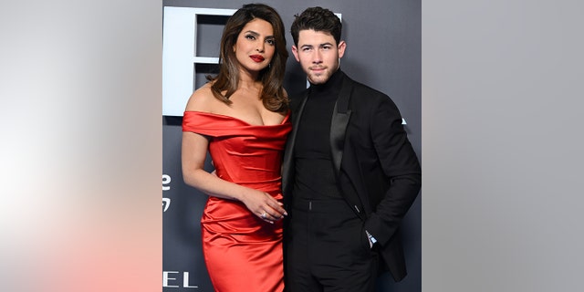Priyanka Chopra in a red form-fitting off-the-shoulder gown poses on the red carpet with husband Nick Jonas in all black at the premiere of the "Citadel" in England