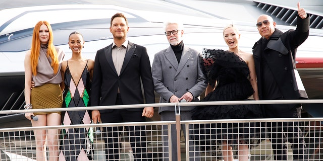 Karen Gillan, Zoe Saldana, Chris Pratt, James Gunn, Pom Klementieff and Vin Diesel stand behind a fence and look out to the crowd at a European gala event at the Avengers Campus in Disneyland Paris while promoting "Guardians of the Galaxy Vol. 3"