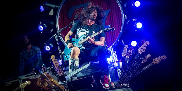 Dave Grohl sitting on his throne onstage rocking out with a guitar with his leg in a boot