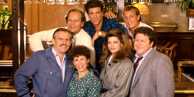 The cast of 'Cheers' smiles in a photo, including Kirstie Alley, Woody Harrelson, Ted Danson, Kelsey Grammer
