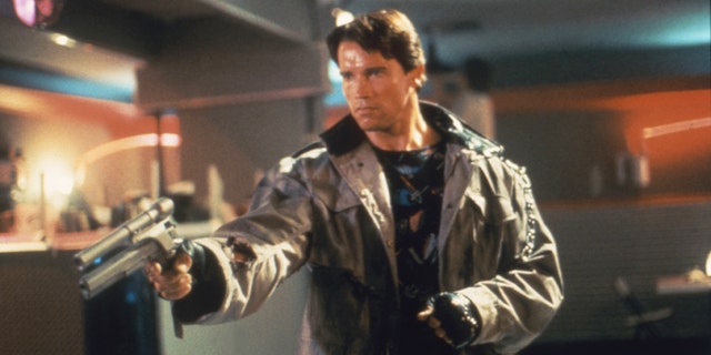 Arnold Schwarzenegger holding a weapon in a scene from "Terminator," where he is wearing a brown leather jacket