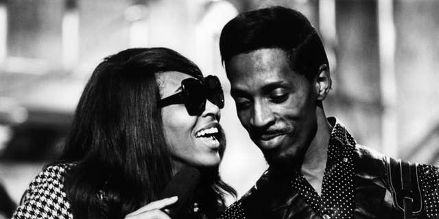Tina Turner performs wearing sunglasses with Ike Turner in black and white photo.