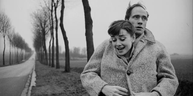 Mel Ferrer envelopes his wife Audrey Hepburn, buttoning her up in his coat, in a picture taken outside Paris in 1956
