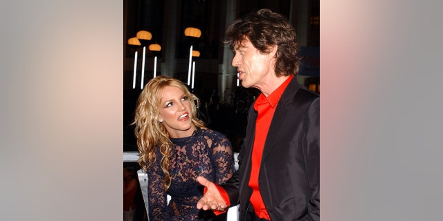 Britney Spears looks hilariously at Mick Jagger as he speaks during an interview at the 2001 VMAs