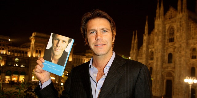 Emanuele Filiberto holding a copy of his book at night in Milan
