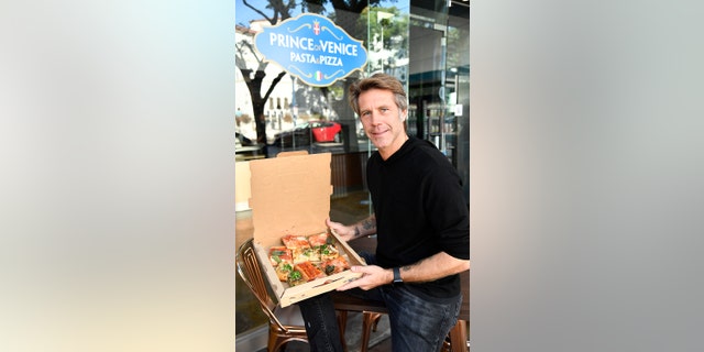 Emanuele Filiberto holding a box of pizza wearing a black sweater