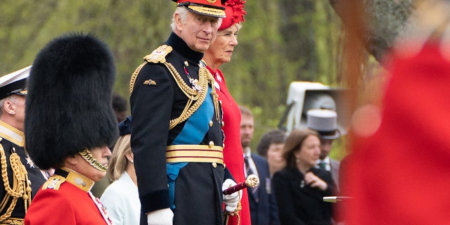 King Charles in a military uniform next to Queen Camilla in a red dress with a matching hat