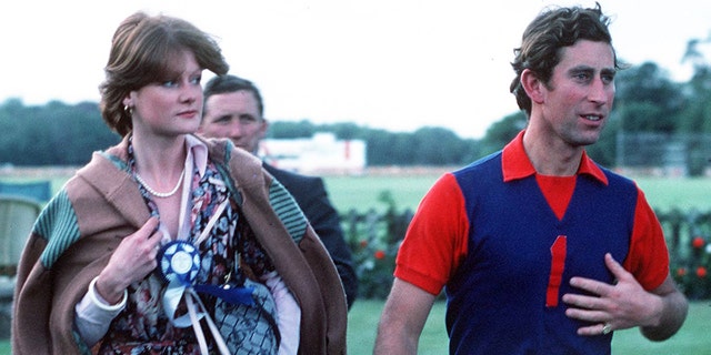 Prince Charles in a blue and red polo shirt walking next to Lady Sarah Spencer in a brightly printed dress