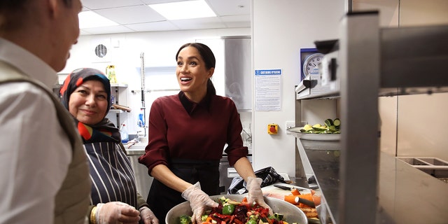 Meghan Markle wearing a burgundy sweater and gloves handling food