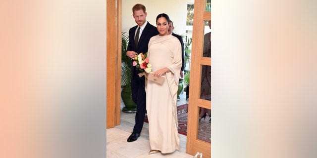 Meghan Markle wearing a creme floor length dress while wearing flowers