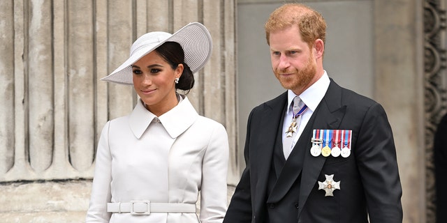 Meghan Markle wearing a white coat dress next to Prince Harry wearing a suit and medals