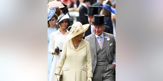 Prince Harry in a top hat and suit next to Meghan Markle in a white dress and a matching hat walking behind Queen Camilla in a yellow dress with a matching hat and King Charles in a grey suit and top hat