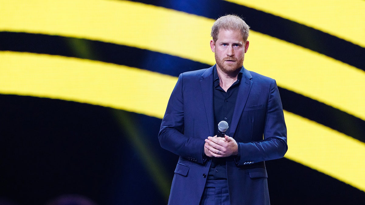 Prince Harry giving a speech and holding a mic in a navy suit