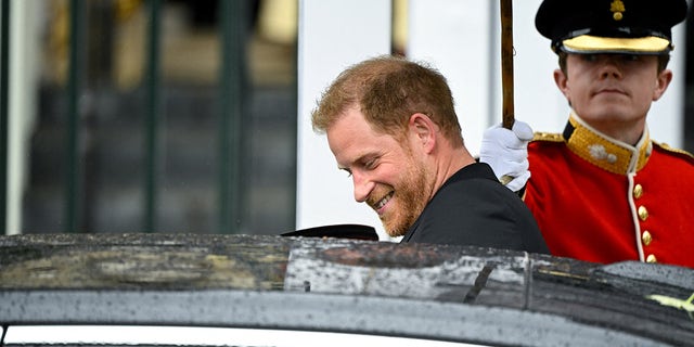 A smiling Prince Harry entering a black car