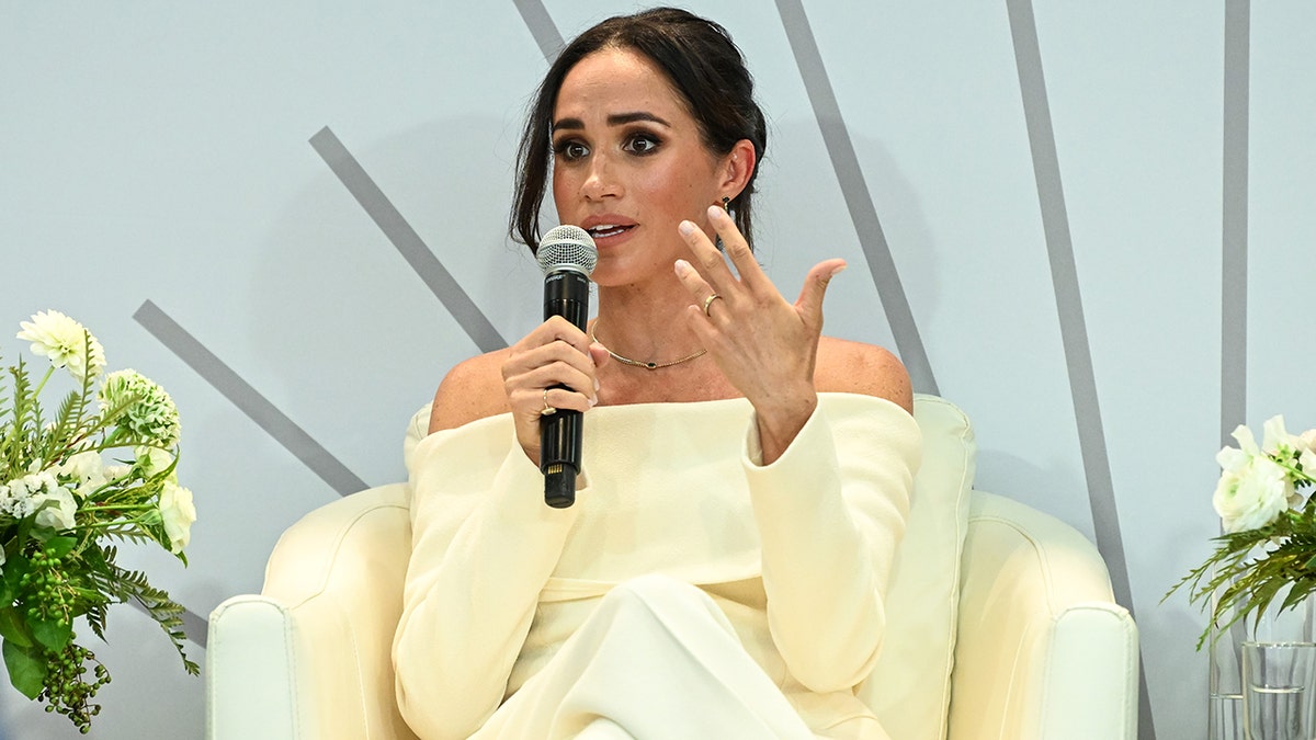 Meghan Markle wearing an ivory sweater speaking to a mic