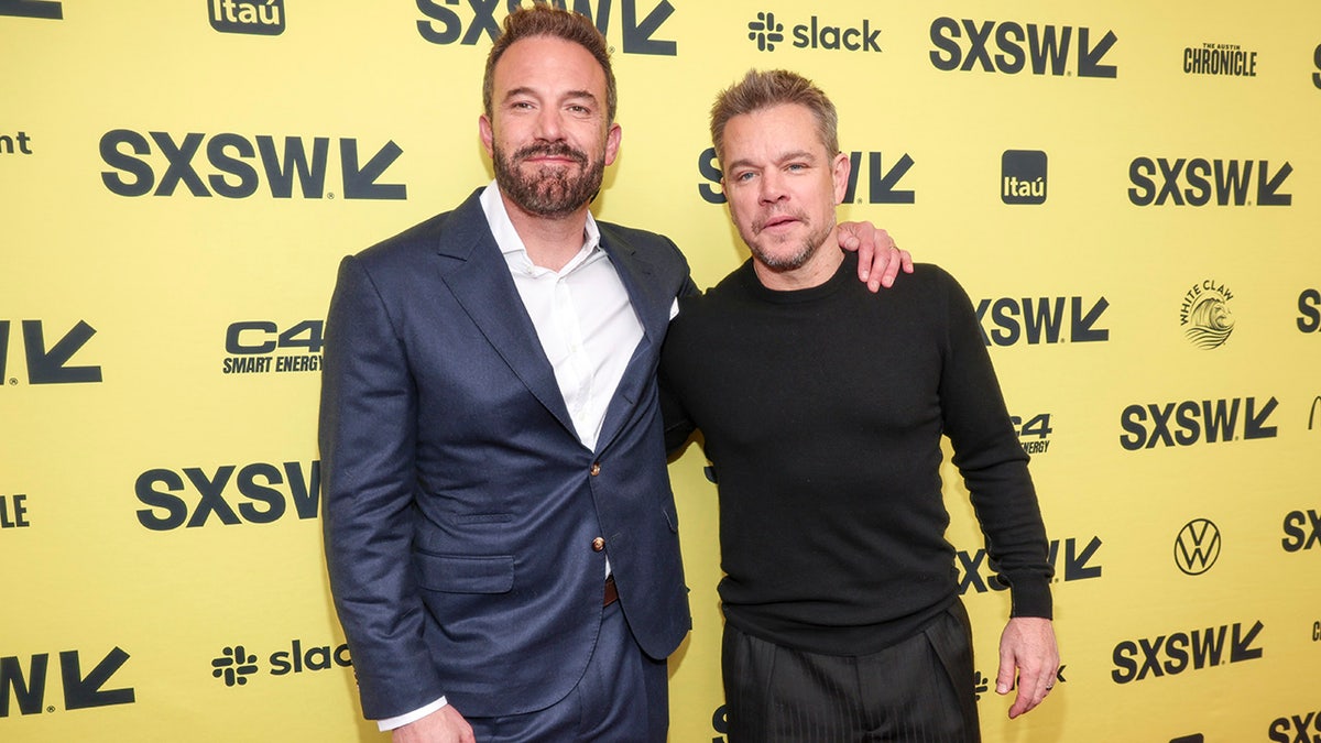 Ben Affleck in a white shirt and blue suit wraps his arm around Matt Damon wearing a black shirt at SXSW
