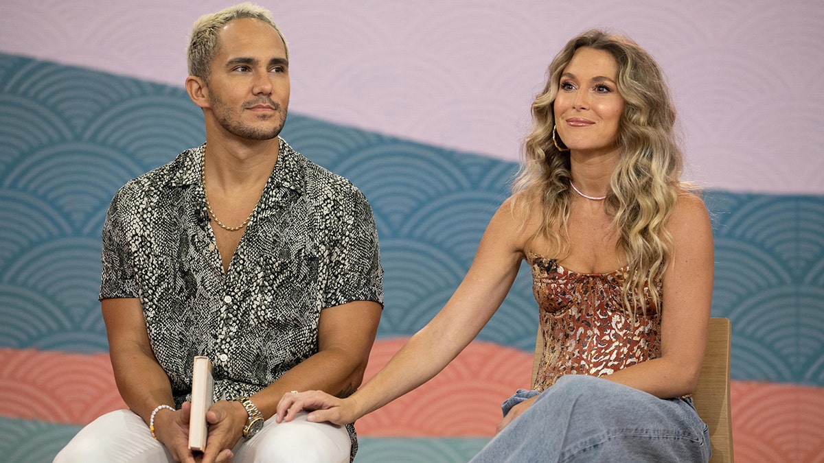 Carlos and Alexa PenaVega sitting next to each other behind a blue and pink background