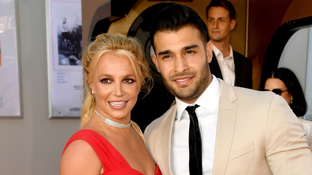Britney Spears in a red dress and Sam Asghari in an off-white/tan suit and black tie