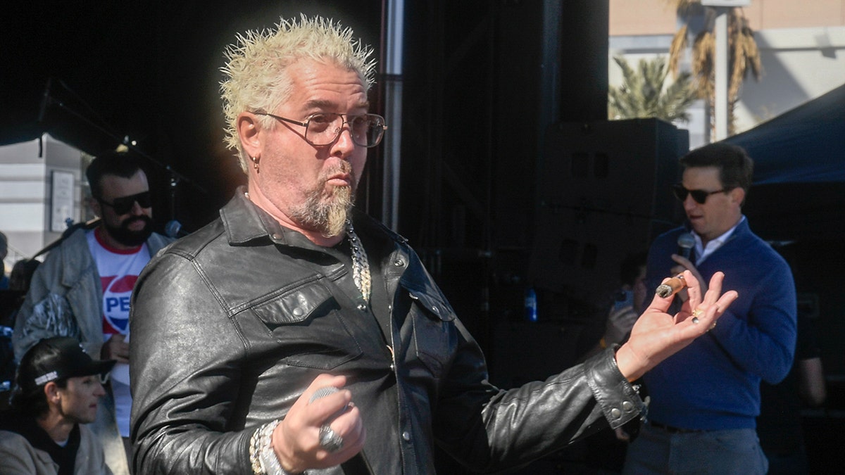 Guy Fieri in a leather jacket making a silly face and sticking his arms out