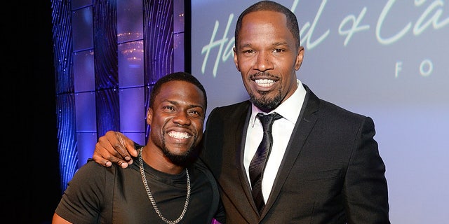 Jamie Foxx wears a black tuxedo with Kevin Hart wearing a black shirt at celebrity event.