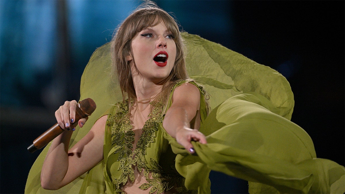 Taylor Swift in a green dress looks up in awe during her Eras concert