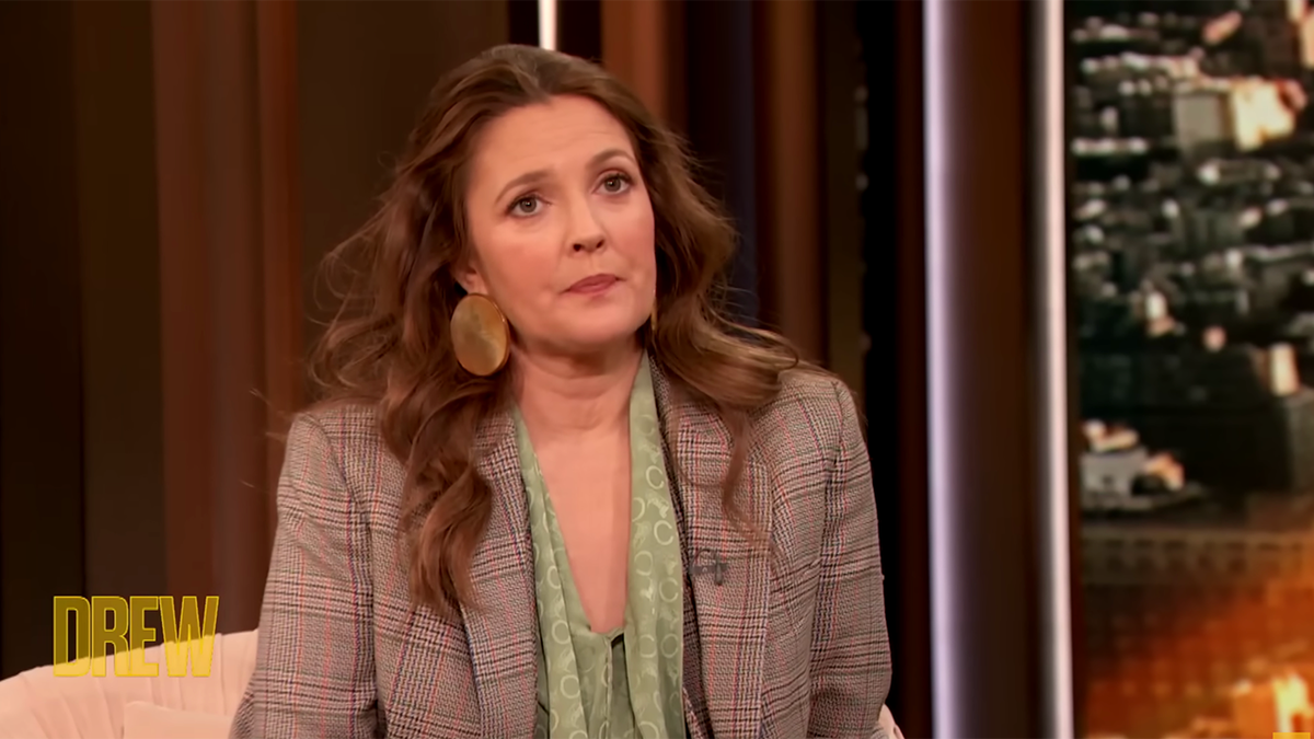 Drew Barrymore in a green blouse and plaid blazer looks up on "The Drew Barrymore" show